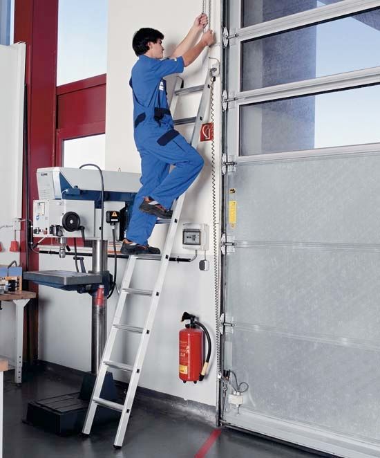Thang Nhôm: Cấp Tải EN 131 Và Rủi Ro Điện 2 Thang tựa dựng nghiêng vào tường để tiếp cận sàn tầng trên của nhà kho